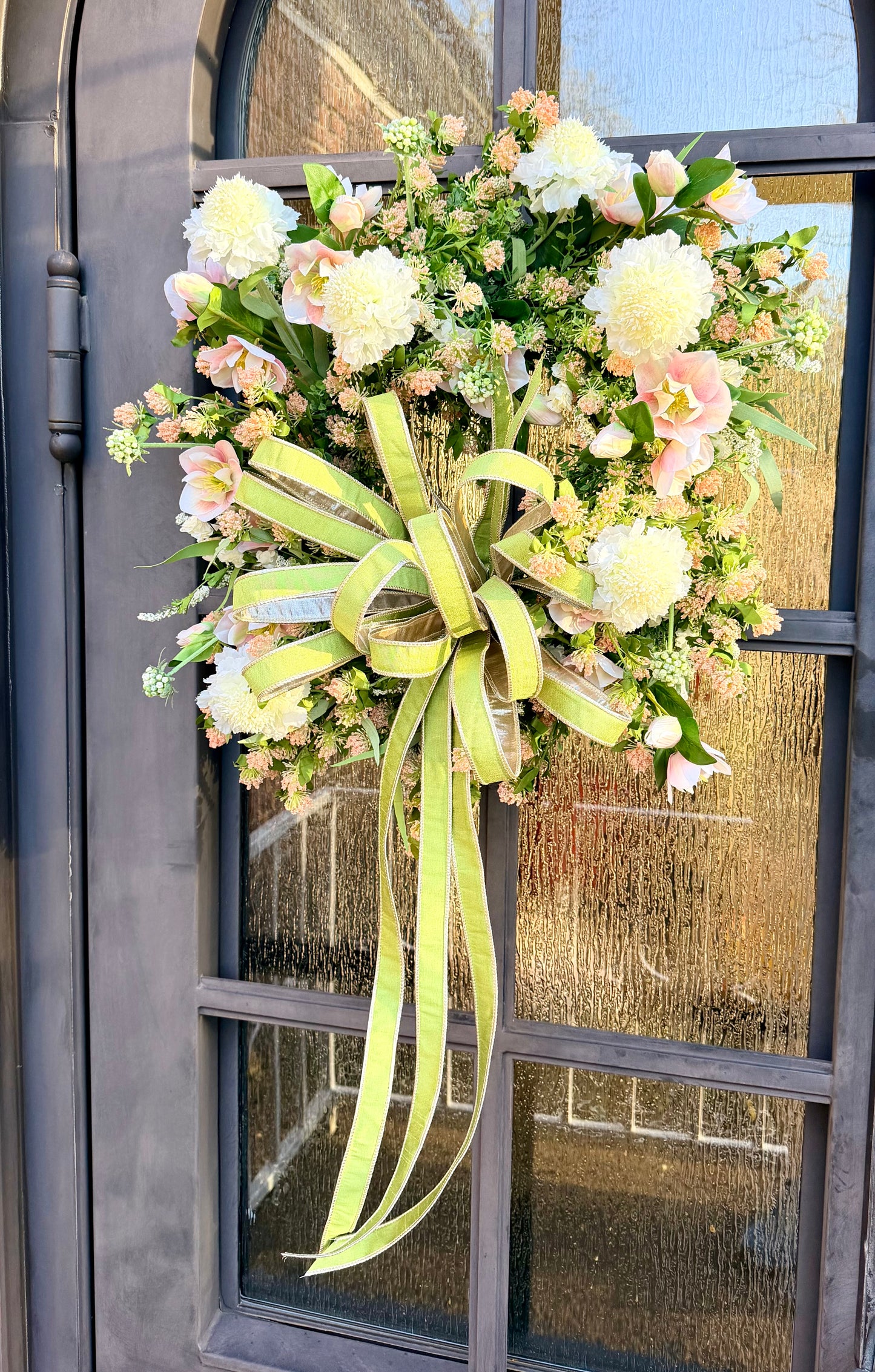 JME handmade wreath of blush, hellebore and white Scabiosa and different mixed florals. Paired with a JME 1 inch green bow. About 24 inches in diameter. 