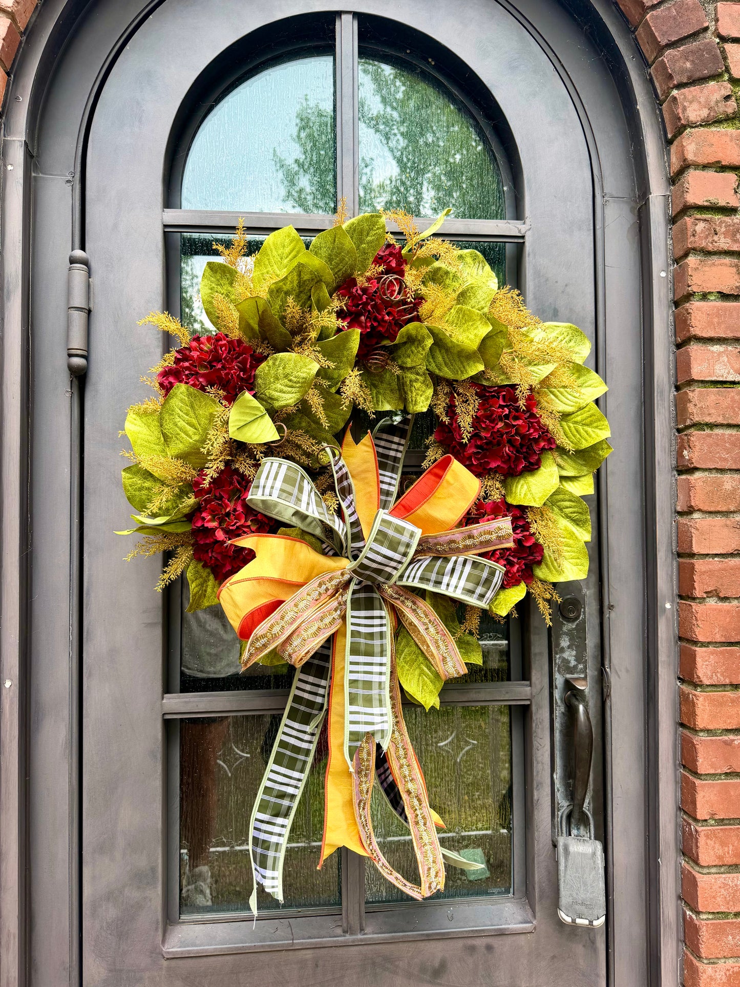 JME HANDMADE WREATH. Magnolia leaves with burgundy hydrangeas and paired with a JME green plaid and jeweled bow. About 32 inches wide. *Some fluffing may be required upon receiving.