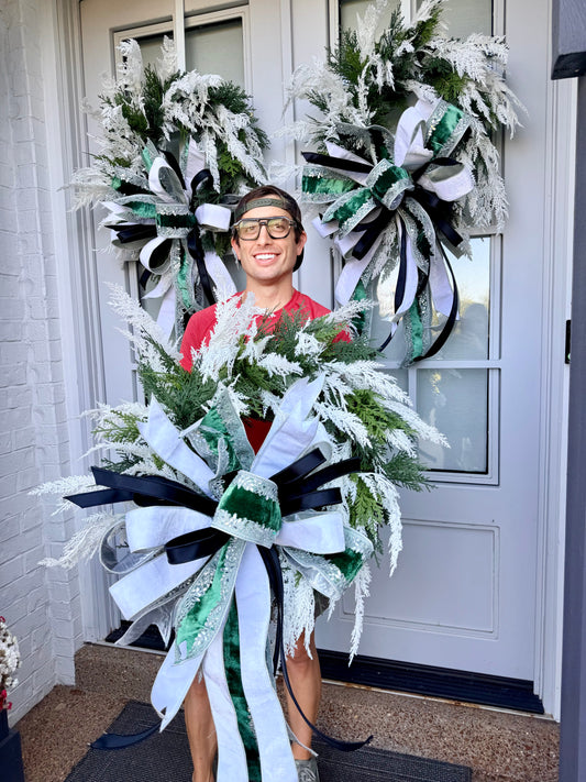 JME Handmade Wreath of cedar and white icy ferns. Paired with a JME hand tied bow of dark green, icy bling, and white velvet and black satin. About 24inches in diameter.