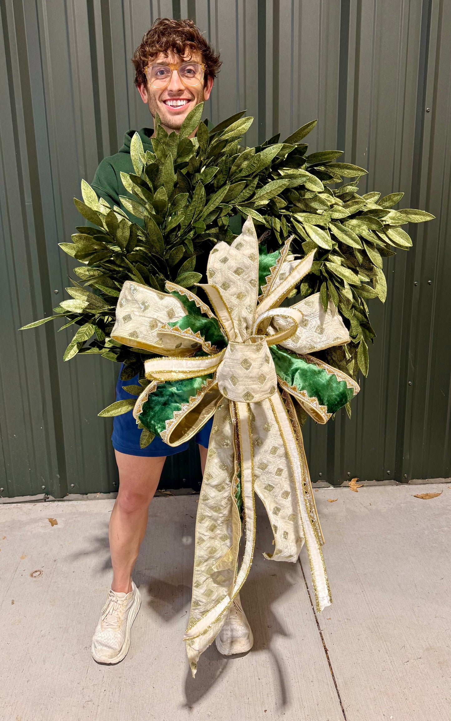 Green and gold faux bay leaf wreath. 30 inches wide. Paired with a JME handtied blue velvet tied bow of white and green velvets.