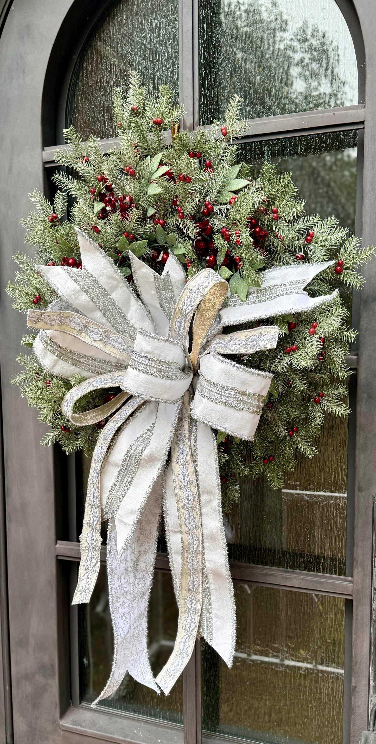 Sweet and soft for the holidays. JME hand made wreath made of red berries, and winter foliage, paired together with a JME hand tied bow of whites, silvers, and holly ribbon. Approximately 24 in.