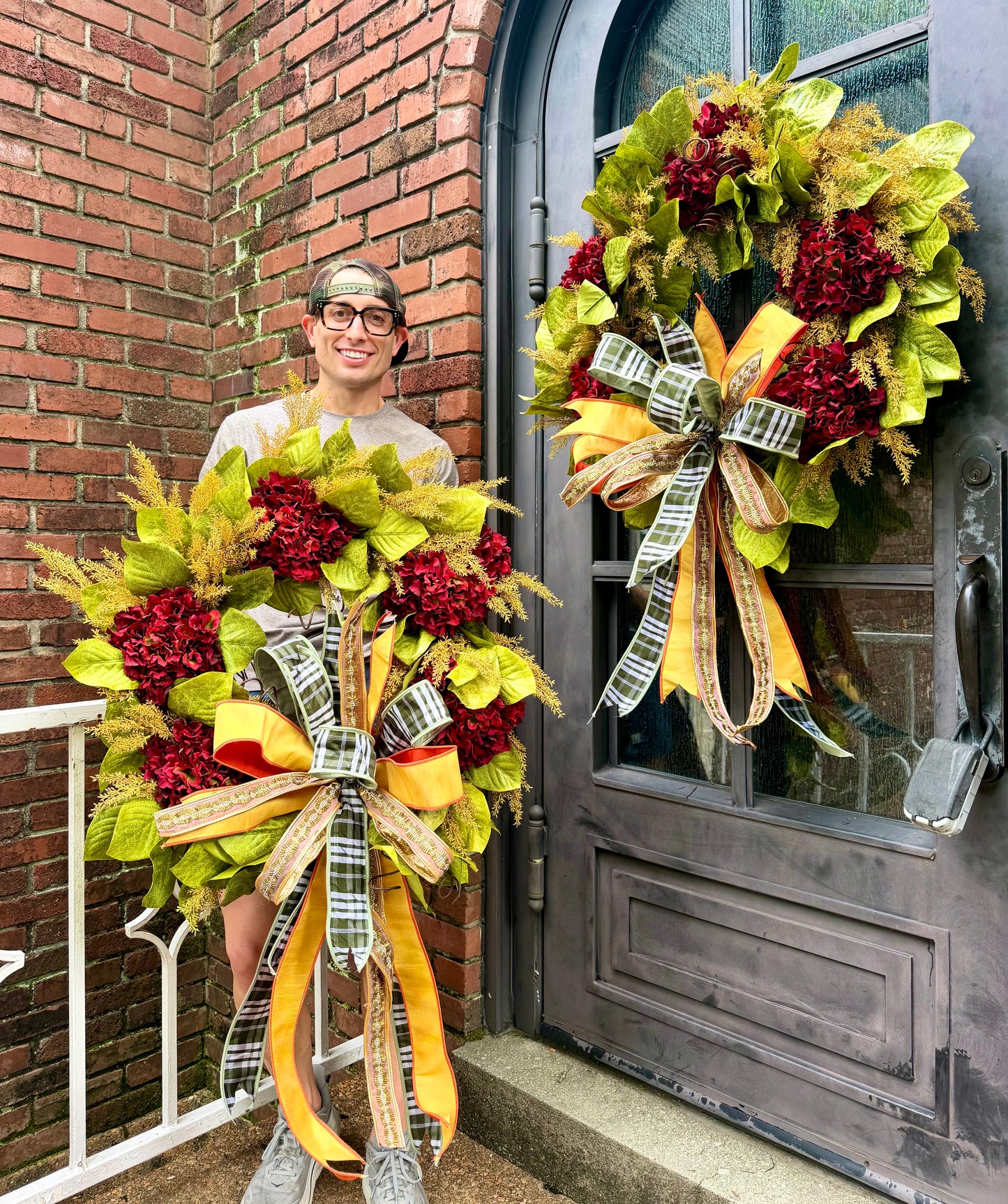 JME HANDMADE WREATH. Magnolia leaves with burgundy hydrangeas and paired with a JME green plaid and jeweled bow. About 32 inches wide. *Some fluffing may be required upon receiving.