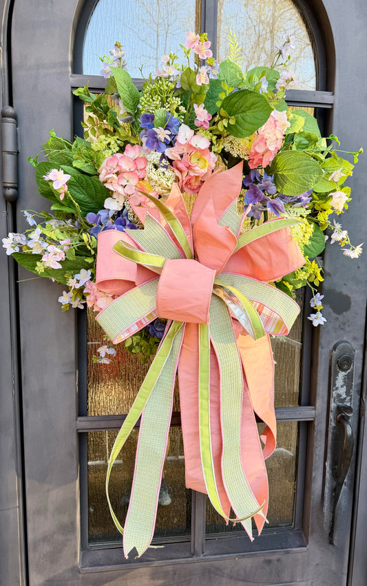 JME mixed hydrangea and wild flower wreath. Paired with a JME hand tied bow of blush and soft spring greens. About 24 inches in diameter.