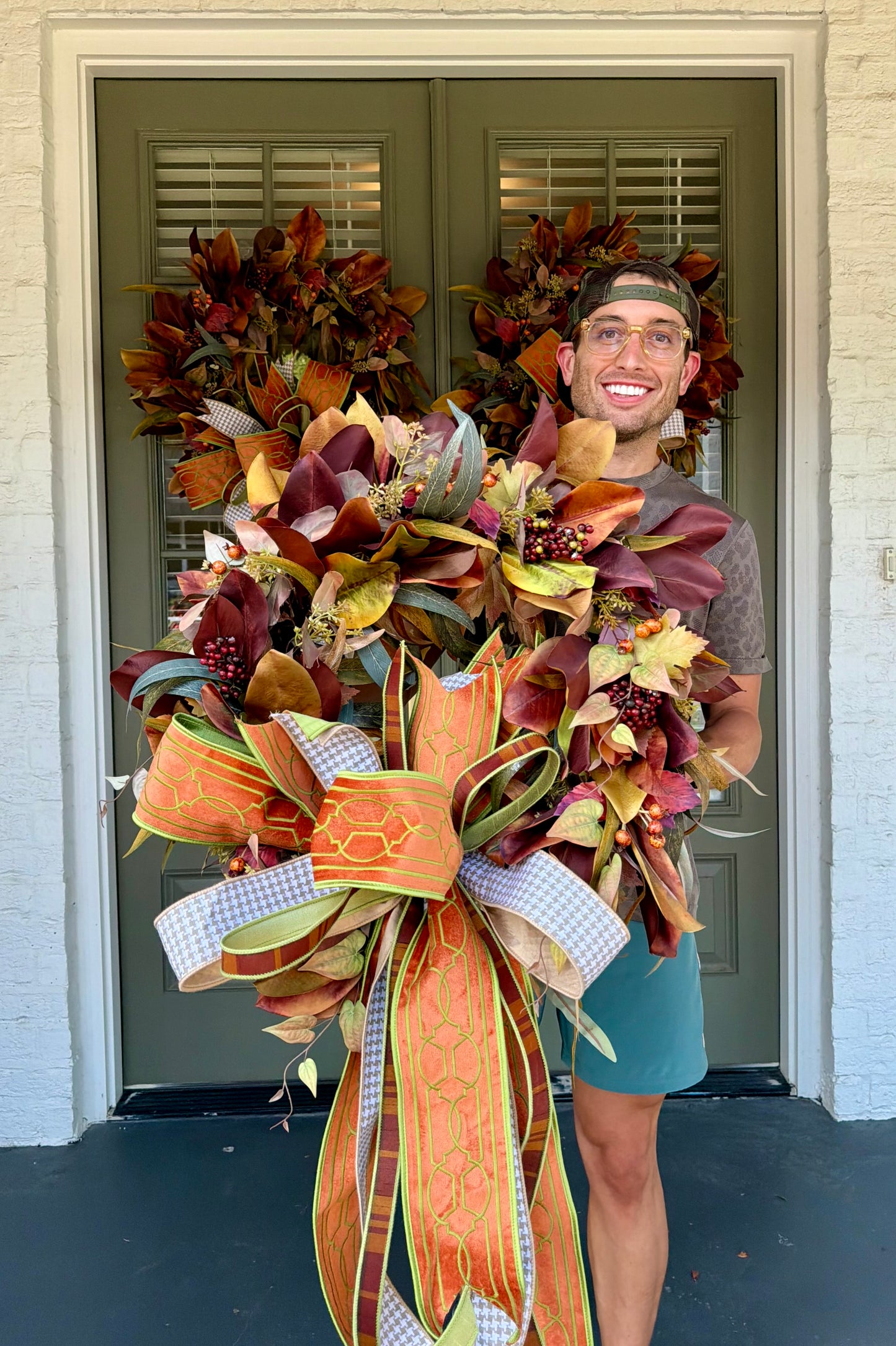 JME fall faux MAGNOLIA WREATH paired with other fall botanicals. About 26inches in diameter. Paired with a JME hand tied bow of orange and browns. Some fluffing may be required upon receiving.