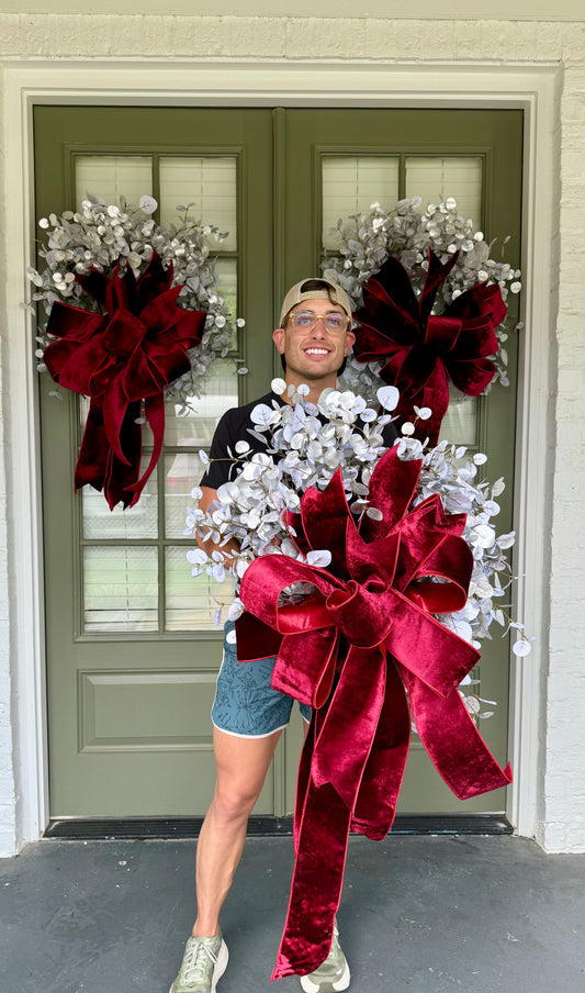 Faux silver eucalyptus wreath with hand tied JME deep red velvet bow. About 24 inches wide.