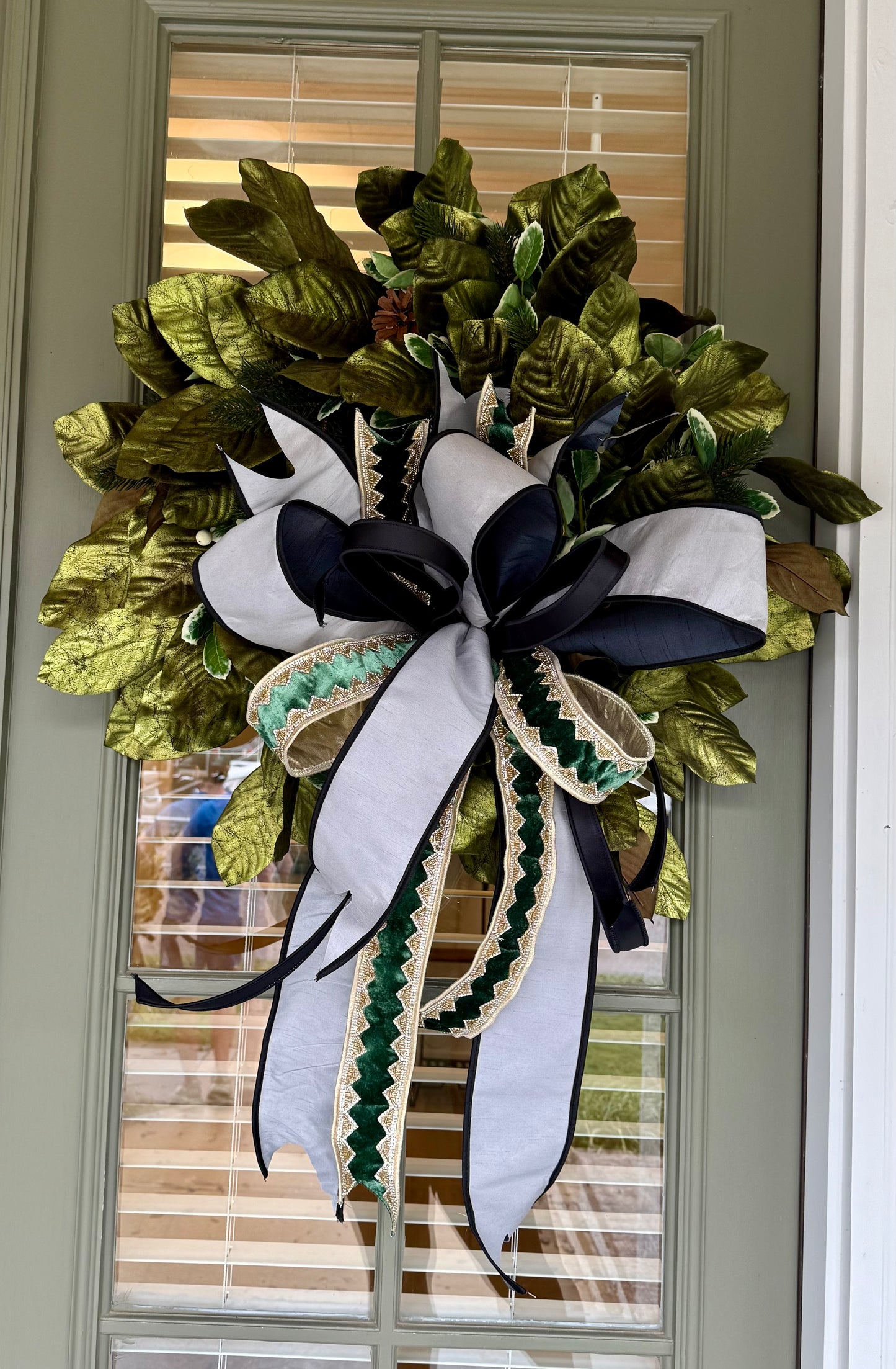 Handmade wreath with metallic green magnolias and a sophisticated JME handtied bow. About 24inches wide.