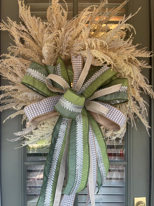 Faux Pampas Grass Wreath paired with a JME hand tied bow featuring a green ribbon with silver leaf embellishment and tan houndstooth ribbon combo. Approximately 28 inches in diameter. Some fluffing may be required upon arrival.