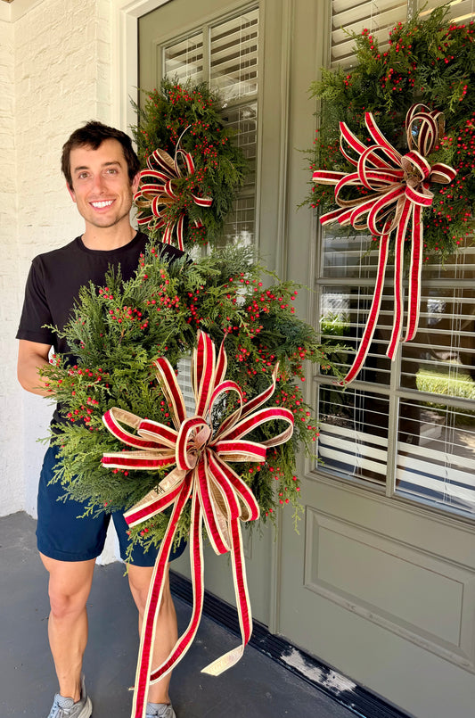 Handmade JME RED BOW wreath of green winter foliage and red berries. Paired with a hand-tied JME 1inch red velvet bow. Approximately 24inches wide.