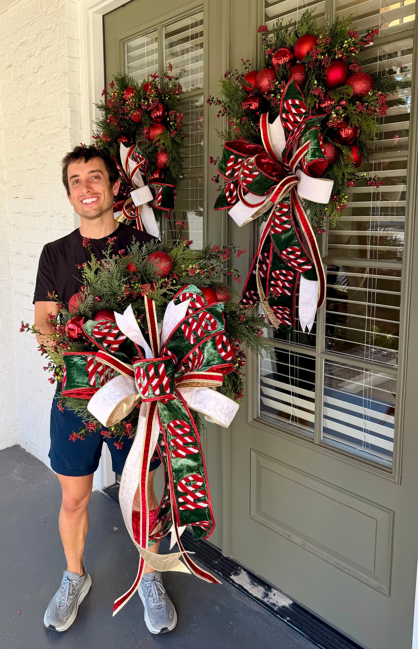 HO HO HO handmade JME wreath of mixed green foliage, red berries, and red ornaments. Paired with  hand tied JME bow.