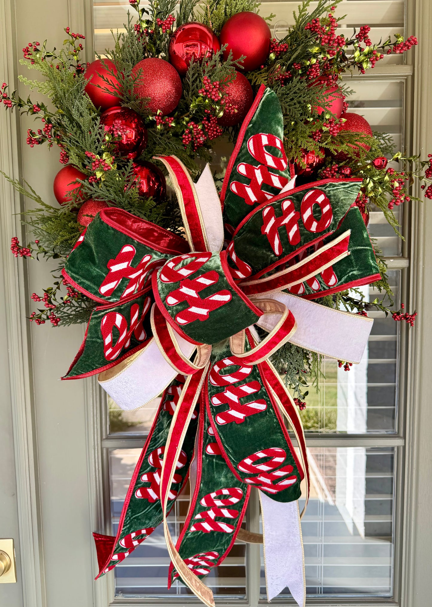 HO HO HO handmade JME wreath of mixed green foliage, red berries, and red ornaments. Paired with  hand tied JME bow.