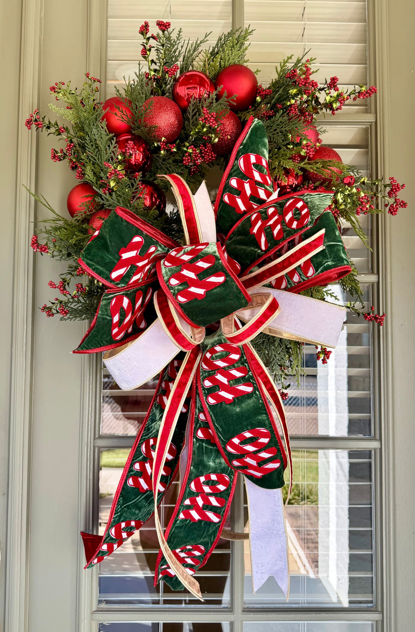 HO HO HO handmade JME wreath of mixed green foliage, red berries, and red ornaments. Paired with  hand tied JME bow.